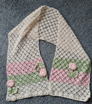 Cream coloured stole with pink and green 3 inch panels at the end after which there is a 3 inch white panel. The green and pink parts have pink flowers with green leaves. This is a crochet product by Triggerfish Crochet.