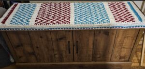 Mosaic horizontal pattern bench cover in red, white and turquoise. The bench is the top part of a wooden cabinet.
